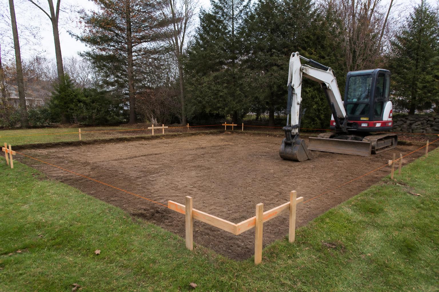 Site prep — string lines and stakes on a cleared backyard building pad